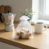 White organza pouch 15x20 cm filled with fudge candies, placed on a wooden top next to a moka pot.