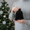 Small black velvet pouch held in hand with Christmas tree lights in the back.