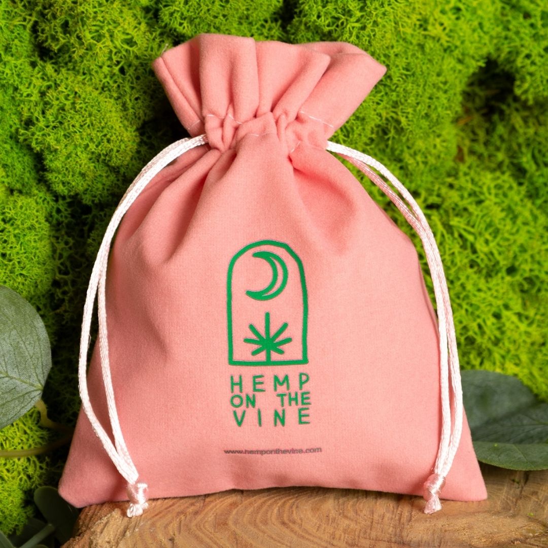 Pink velvet pouch with green plant pattern and logo.