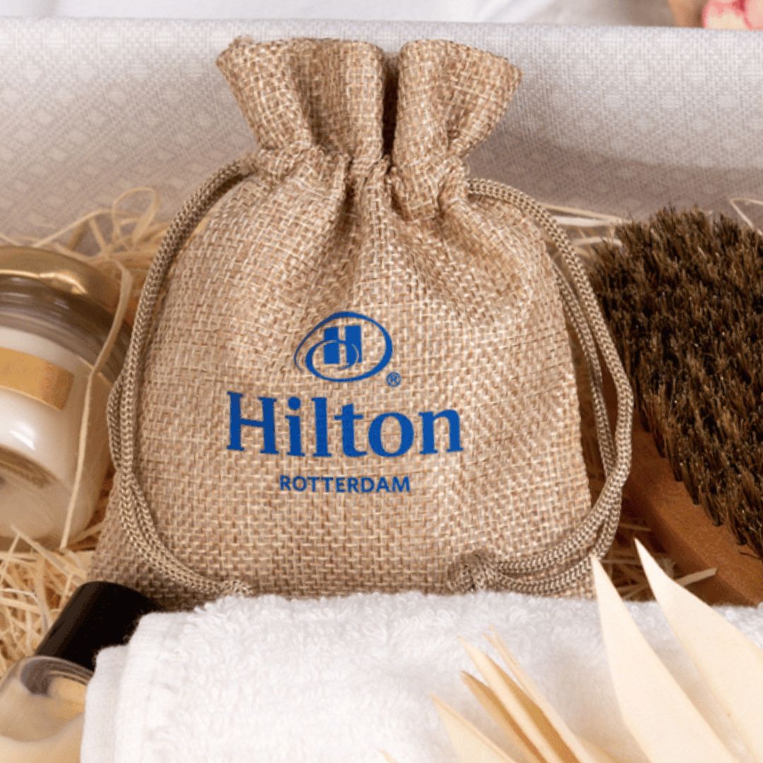 Jute pouch with blue Hilton logo, placed on a towel.