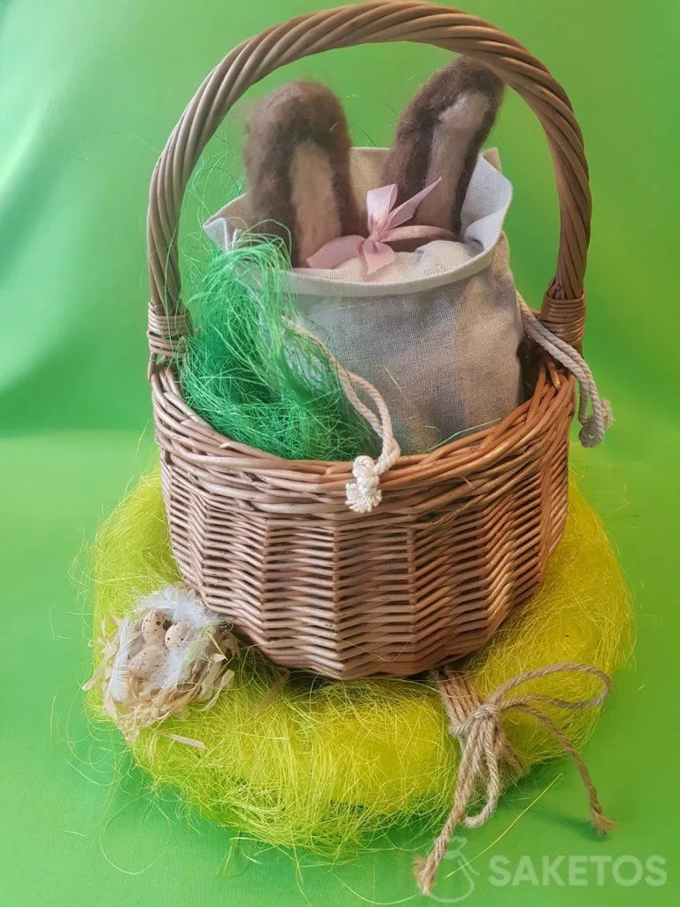 Basket with a linen pouch from which the ears of a felt worsted bun are protruding.